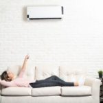 Woman on a sofa pointing at an air conditioning unit, showcasing home comfort from Walker Plumbing, Heating & Air.