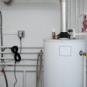Water heater in utility room with exhaust pipe and hose. Featured services from Walker Plumbing, Heating & Air.