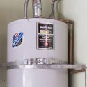 Gray metallic water heater with circular shape and pipes, featuring manufacturer's label and energy efficiency sticker.