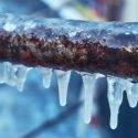 Icicles hanging from a rusty pipe outdoors, illustrating winter conditions relevant to HVAC maintenance tips.