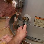 Hand holding a valve near water heater and piping, showing maintenance work by Walker Plumbing, Heating & Air.
